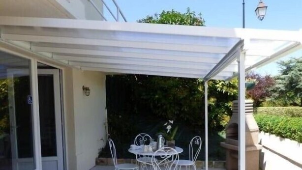 A covered patio with a table and chairs, a pergola, and a view of the surrounding greenery.