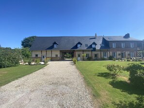 A two-story house with a central entrance and symmetrical facade, set amidst a well-manicured lawn and gravel driveway.