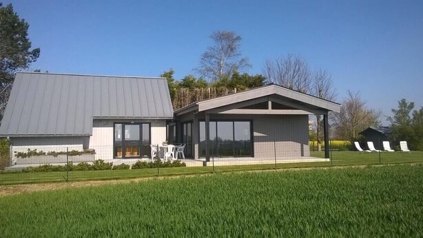 Una casa moderna con un amplio patio, un espacio exterior cubierto y un césped bien cuidado.