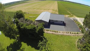 Un edificio grande con techo plano, rodeado de campos verdes y árboles.