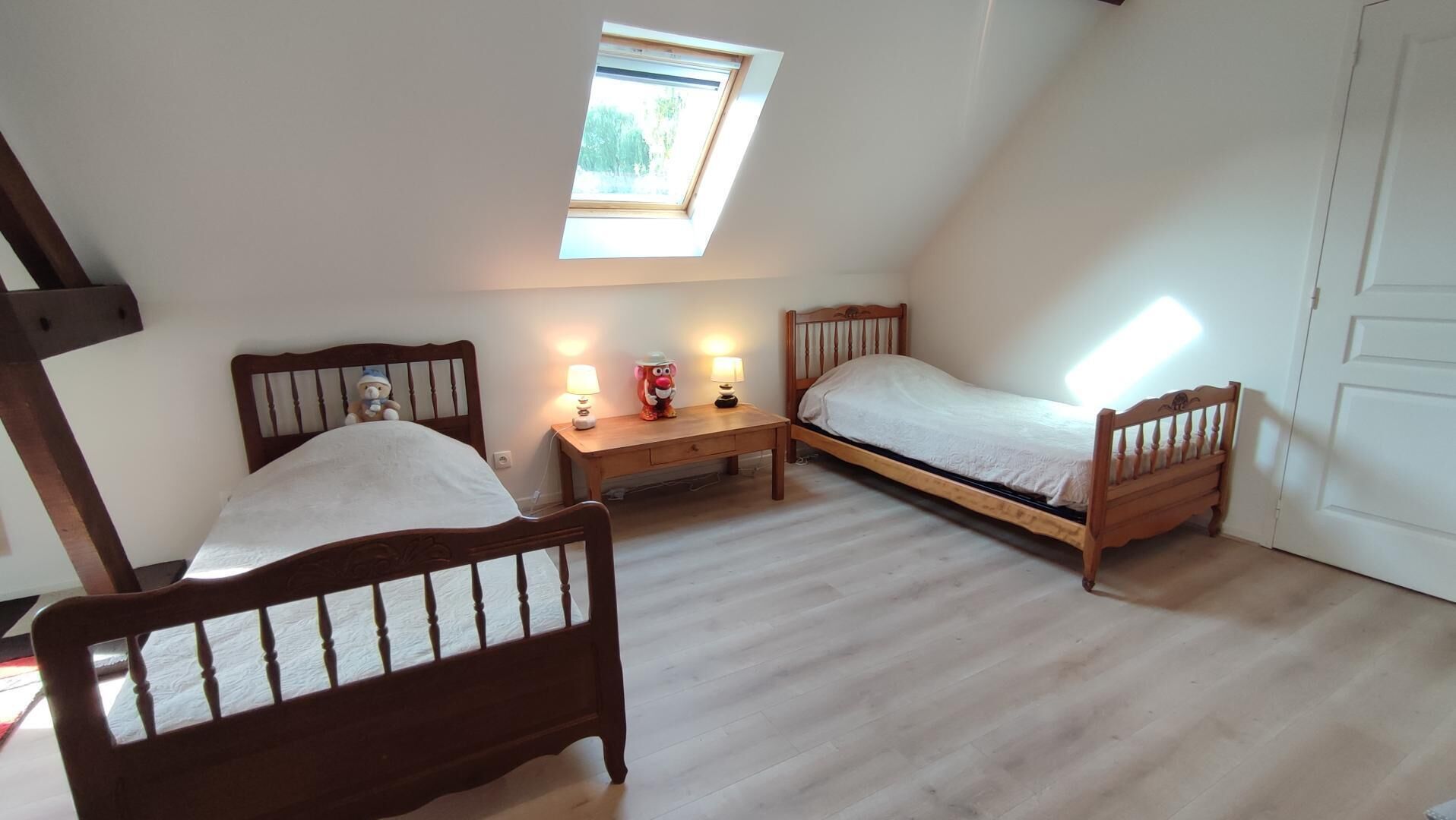 Une petite pièce bien éclairée, avec deux lits en bois, une table de chevet et une lucarne.