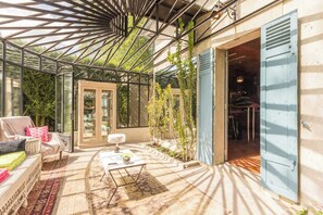 A conservatory with a glass ceiling, a seating area with a sofa and armchairs, a coffee table, and a door leading to an interior space.