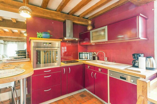 A compact kitchen with red cabinets, a stainless steel oven, a microwave, and a sink.