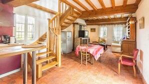 A rustic kitchen with a wooden staircase, a dining area with a table and chairs, and a living room with a sofa and a chair.