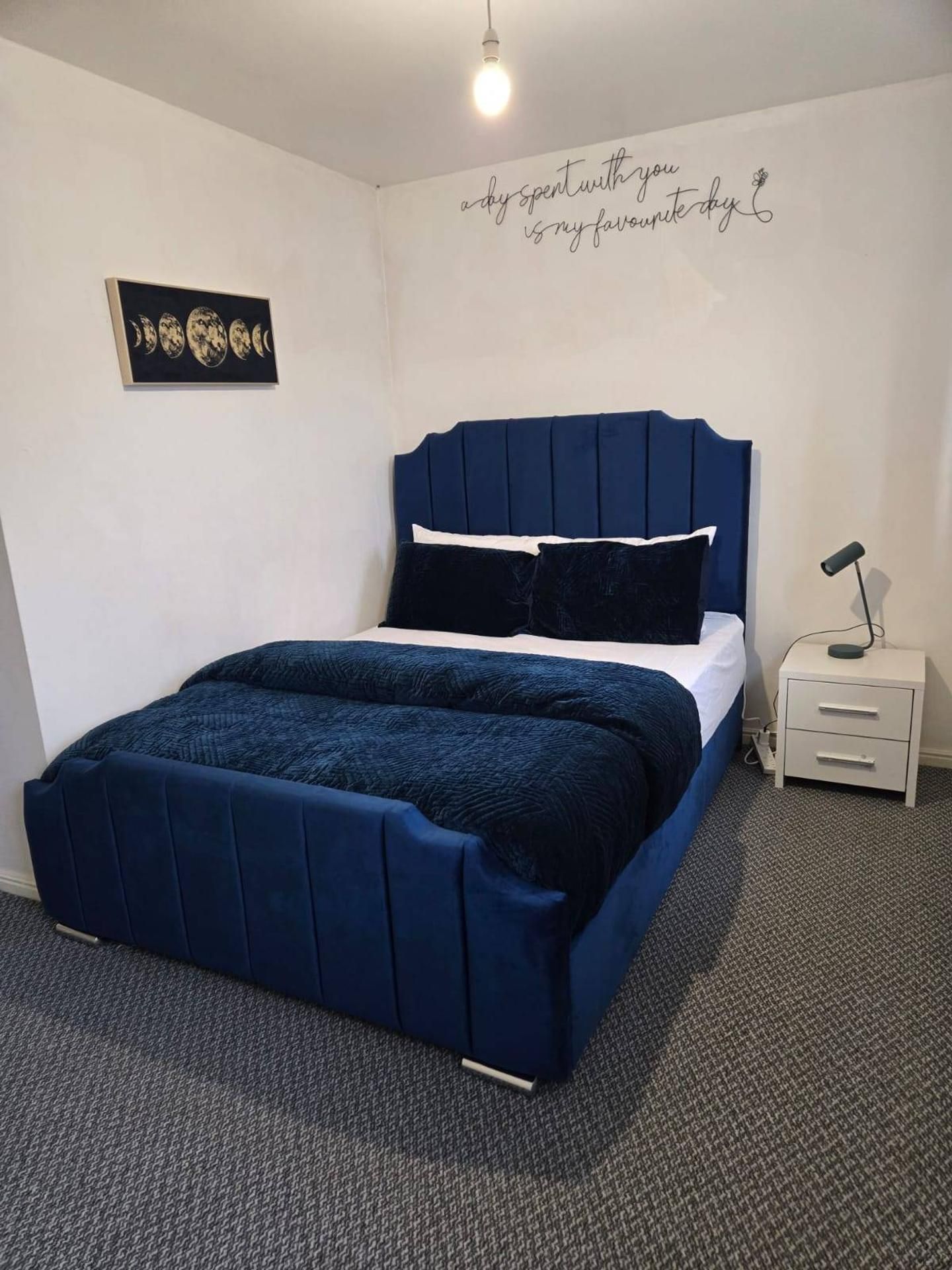 Un dormitorio con cama, mesita de noche, lámpara y un adorno en la pared.