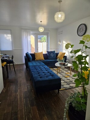 Een woonkamer met een donkerblauwe bank, een passende voetenbankje, een salontafel en een potplant.