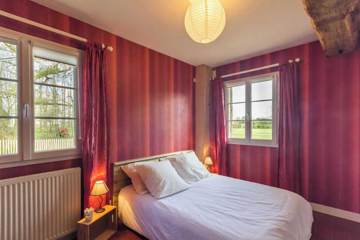 Une chambre à coucher comprenant un lit, deux tables de chevet, une commode, une fenêtre avec des rideaux et un radiateur.