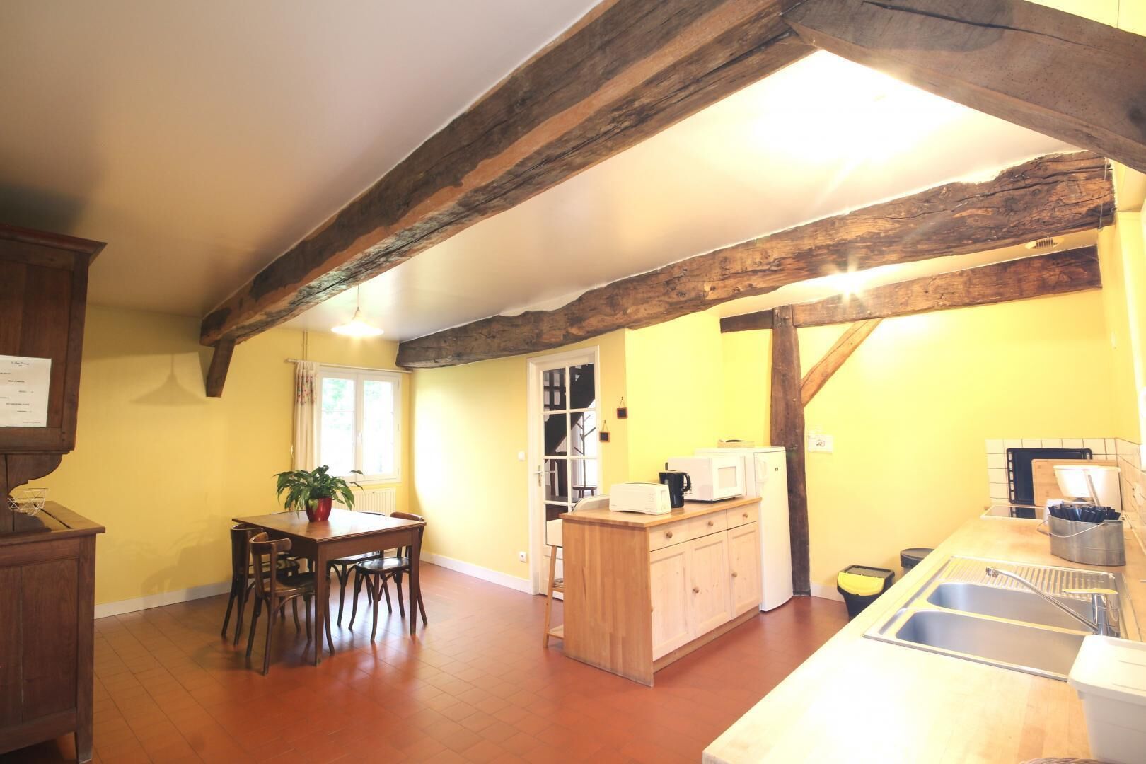 A kitchen with wooden beams, a dining table with chairs, a small island with a sink, and a microwave.