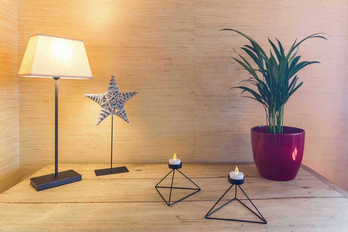 A wooden floor with a floor lamp, a star-shaped decoration, a potted plant, and two candle holders.