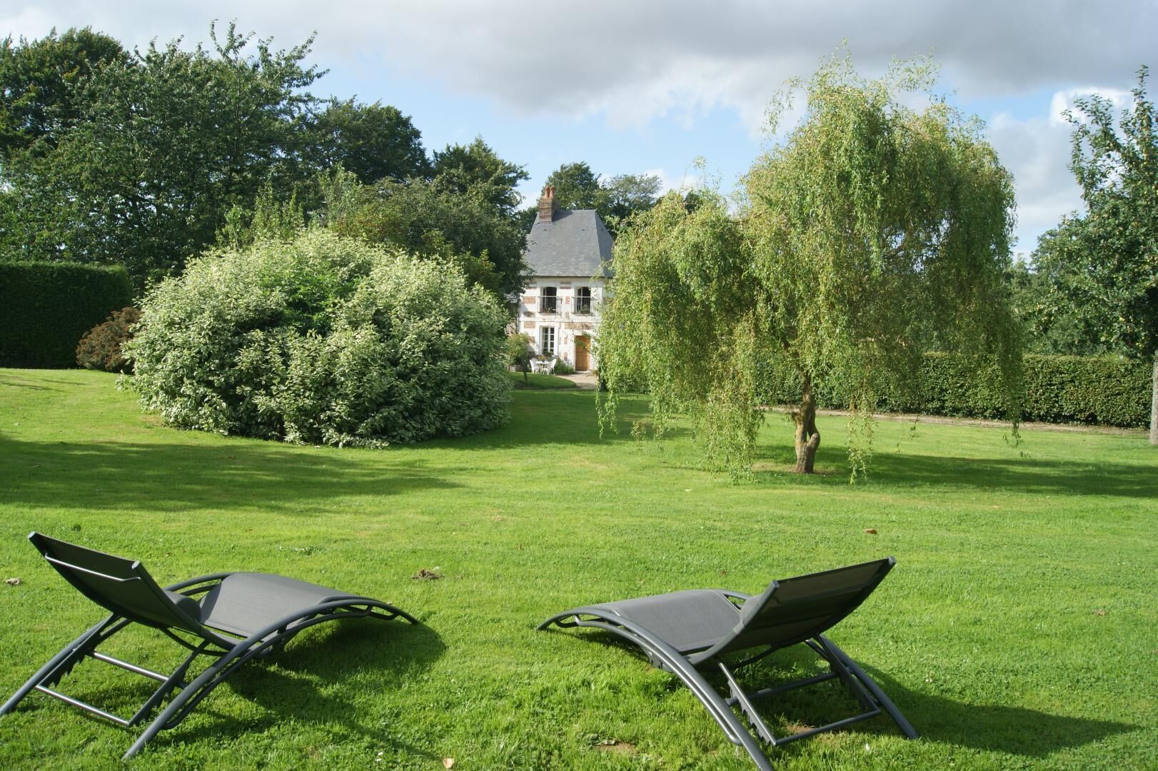 Een verzorgd gazon met twee lounge stoelen gericht op een groot huis met een grijs dak en een rode deur.