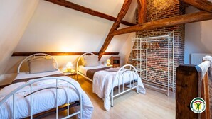 Ein gemütliches Schlafzimmer im Dachgeschoss mit drei Metallbetten, Holzbalken und einer Ziegelwand.