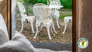 Blick auf einen Garten mit einem weißen Tisch und Stühlen im Freien, einem Sonnenschirm und einem Liegestuhl.
