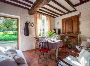 A dining area with a round table set for four, a fireplace, and a view of the garden. - Gîtes de France® - Le Puits (BRETTEVILLE DU GRAND CAUX)