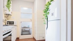 A kitchen with a white stove, microwave, and refrigerator, a door with frosted glass panels, and a tiled backsplash. - MOT Borges 2200 (Buenos Aires)