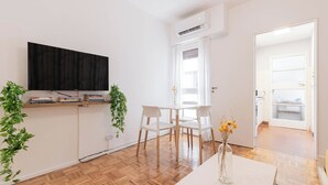 A modern living room with a flat-screen TV, a dining table with chairs, a potted plant, and a vase with flowers. - MOT Borges 2200 (Buenos Aires)