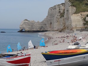 A beach with boats, a rocky cliff, and people. - Gîtes de France® - La Roselière (ST AUBIN ROUTOT)