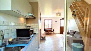 A modern kitchen with a built-in stove, a sink, and a dining area with a table and chairs. - Gîtes de France® - La Normandeuse (REALCAMP)