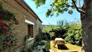 A brick house with a small garden, a wooden table, and two chairs. - Gîtes de France® - La Normandeuse (REALCAMP)