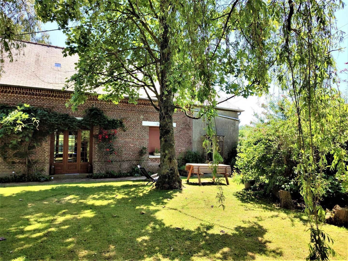 Een bakstenen gebouw met een grote boom in de voortuin, een houten bankje en een gazon.