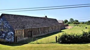 A long, narrow barn with a sloped roof, surrounded by a fenced grassy area. - Gîtes de France® - La Normandeuse (REALCAMP)