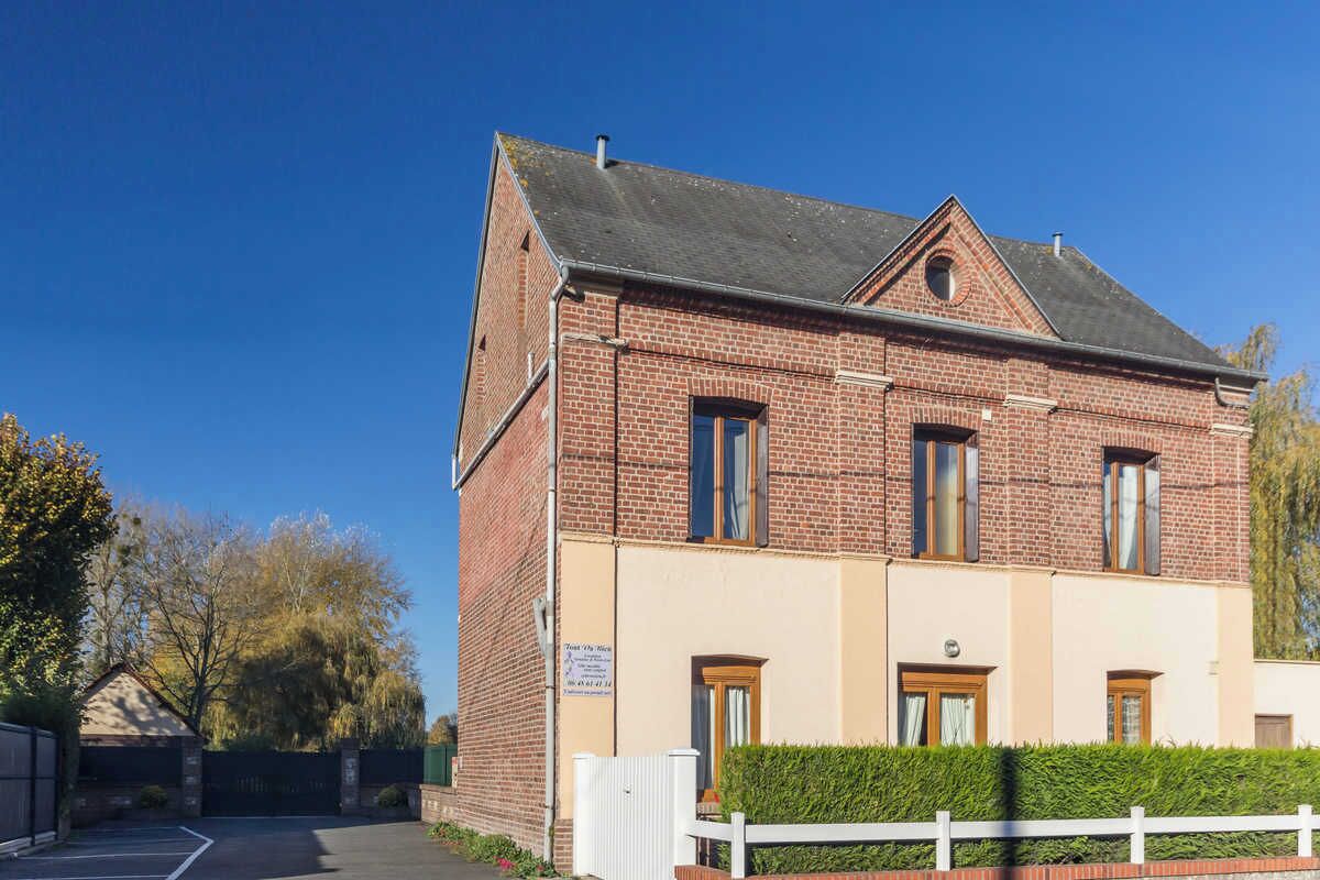 Een tweelaags bakstenen gebouw met een beige gevel, een klein terras en een witte hekken voor.