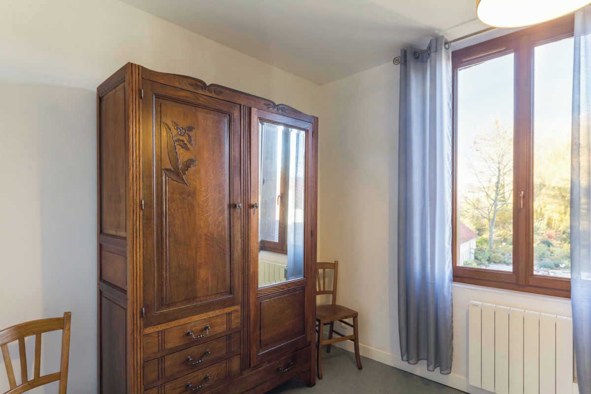 A room with a large wooden wardrobe, a chair, and a window with curtains.