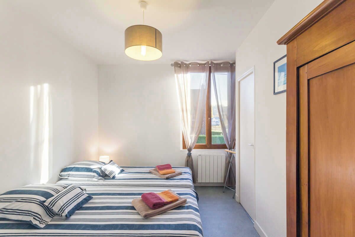 A bedroom with a bed, a radiator, a window with curtains, and a wooden wardrobe.