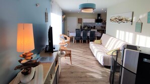 Una sala de estar con sofá, televisión, lámpara y un comedor con sillas y mesa.