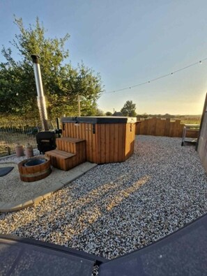 A hot tub area with a wooden deck, a fire pit, and a grill.