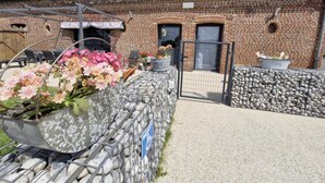Edificio de ladrillo con camino de grava, una reja metálica y un macizo de flores rosadas.
