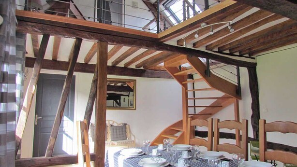 A dining area with a table set for four, wooden beams, and a staircase.