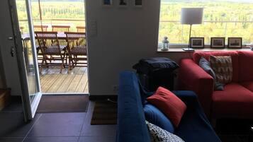 A living room with a blue sofa, red armchair, and a view of a wooden deck and greenery outside.