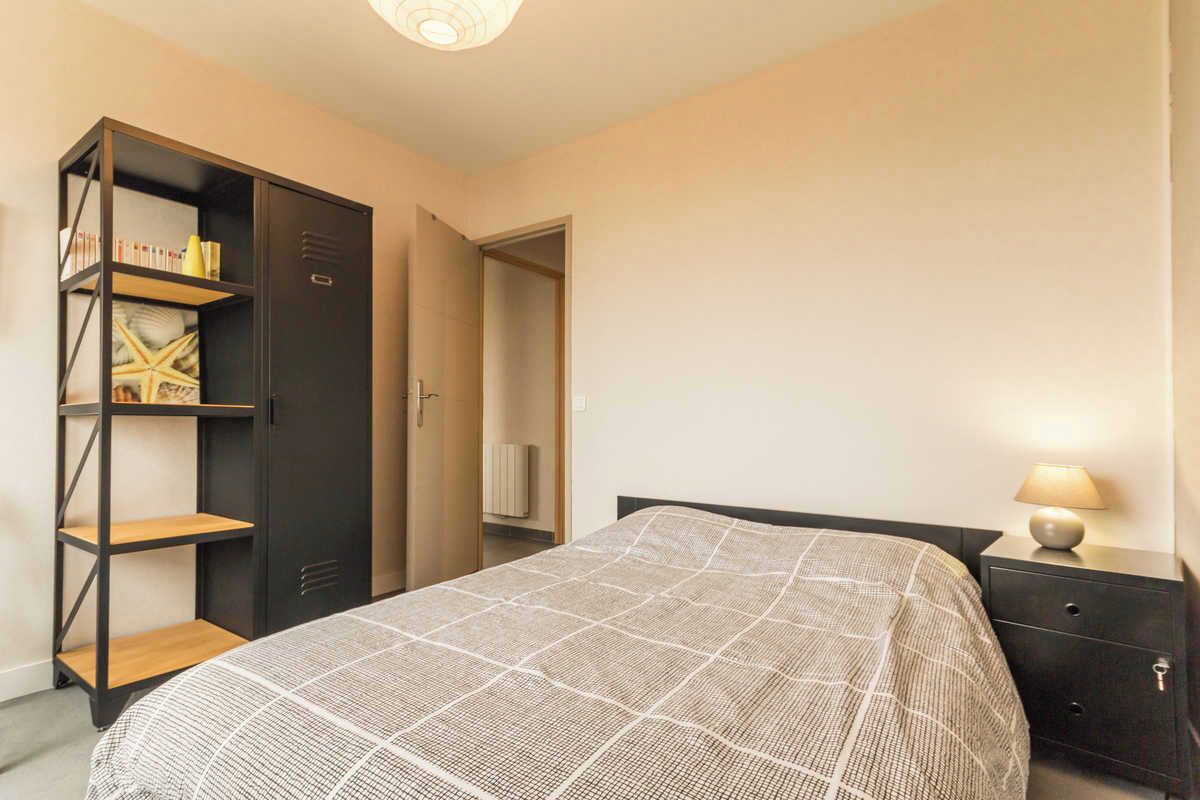 A bedroom with a bed, a wardrobe, a bedside table, and a lamp.