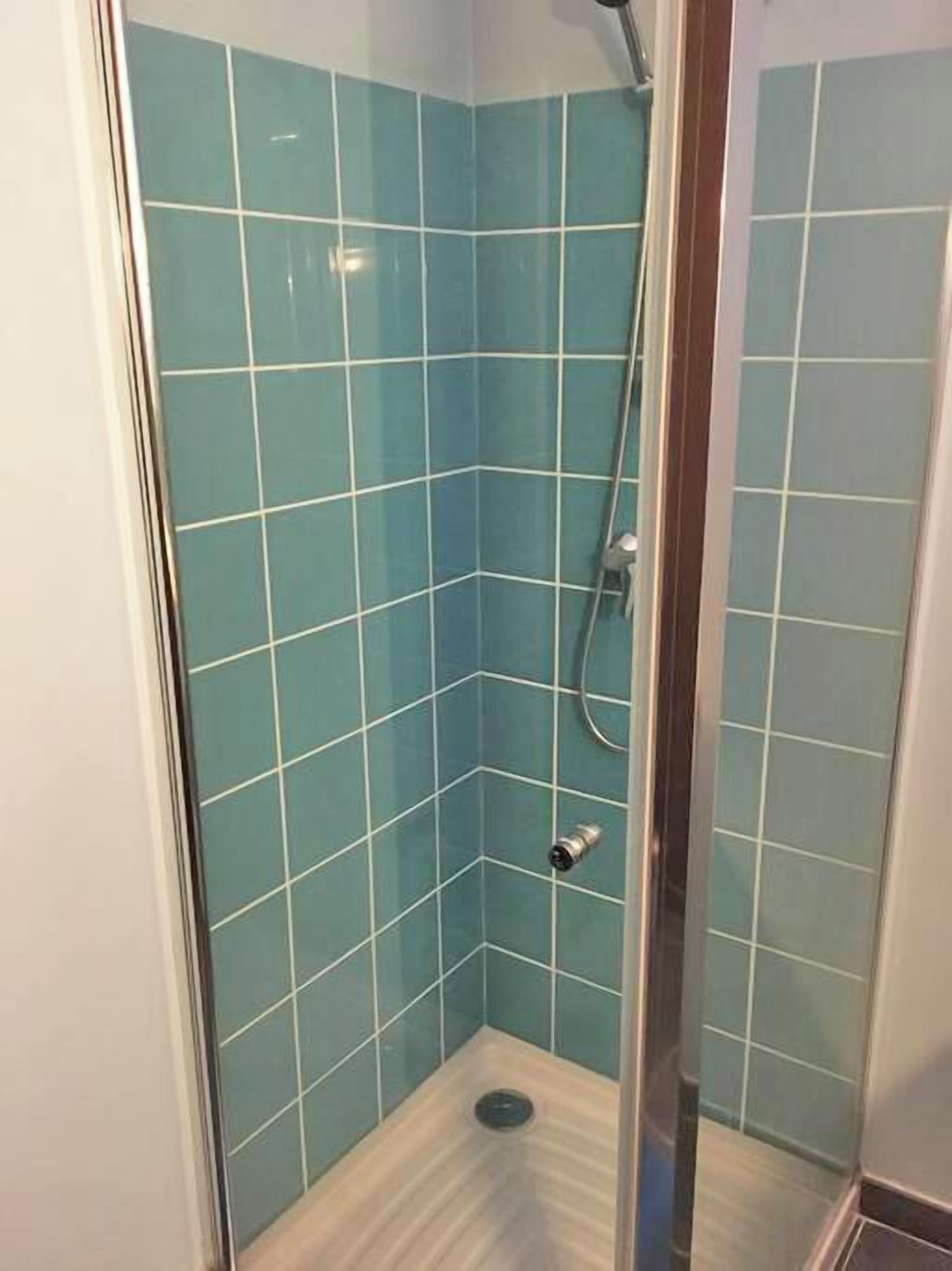 A small, enclosed shower area with blue tiles and a glass door.