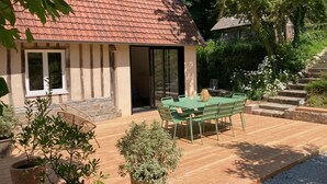 Una casa con techo de tejas, un patio con mesa y sillas, y plantas en macetas.