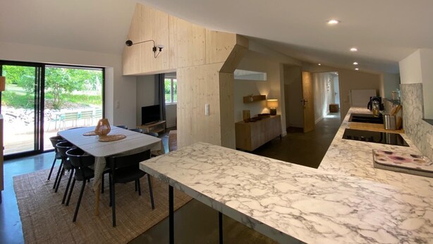 Una cocina moderna con encimera de mármol, un comedor con mesa y sillas, y vistas al exterior.