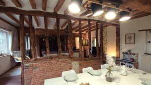 A dining area with a brick wall and wooden beams, a white table set for a meal, and a small white rabbit figurine on the table. - Gîtes de France® - Jacquotte's Chaumière (LIMPIVILLE)