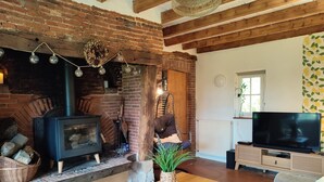 A cozy living room with a brick fireplace, a TV, and a comfortable seating area. - Gîtes de France® - Jacquotte's Chaumière (LIMPIVILLE)
