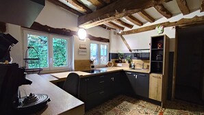 A kitchen with exposed wooden beams, a central island, black cabinets, and a patterned floor. - Gîtes de France® - Jacquotte's Chaumière (LIMPIVILLE)