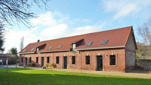 A brick building with a red-tiled roof, multiple windows, and a grassy lawn in front. - Gîtes de France® - Louis-Philippe (BAROMESNIL)