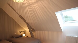 A bedroom with a sloped ceiling, a skylight, a bed, a nightstand, and a lamp. - Gîtes de France® - Louis-Philippe (BAROMESNIL)