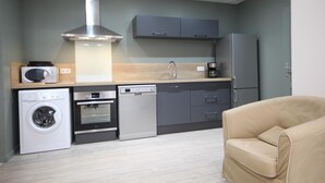 A compact kitchen with a washing machine, oven, dishwasher, and a microwave on the countertop. - Gîtes de France® - Louis-Philippe (BAROMESNIL)