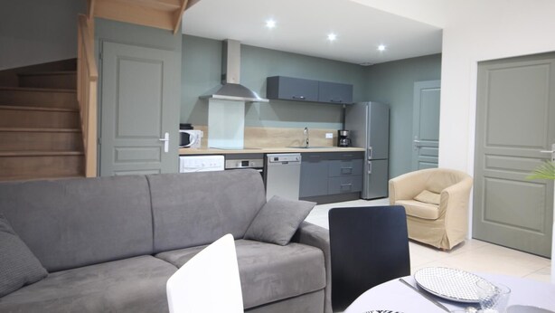 A modern apartment with a grey sofa, a dining table, a kitchen area with grey cabinets, and a staircase. - Gîtes de France® - Louis-Philippe (BAROMESNIL)