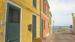 A row of colorful buildings with green shutters, a stone wall, and a view of the sea. - The Grottino (Stintino)