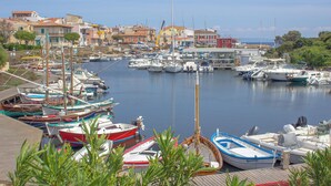 A marina with various boats docked, surrounded by buildings and greenery. - The Grottino (Stintino)
