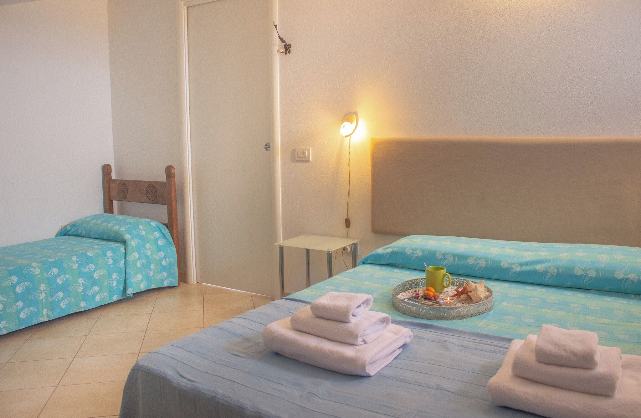 Ett hotellrum med två separata sängar, ett litet bord, en vägglampa och ett dekorativt bricka med ett ljus.