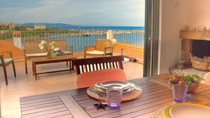 A balcony with wooden furniture, a table with a placemat, and a view of a marina and distant mountains. - The Grottino (Stintino)