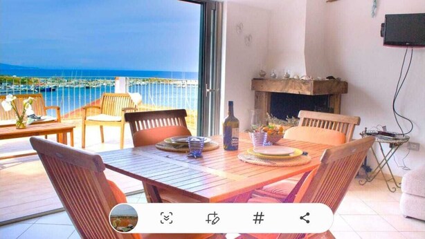 A dining area with a table set for four, a fireplace, and a view of the sea. - The Grottino (Stintino)