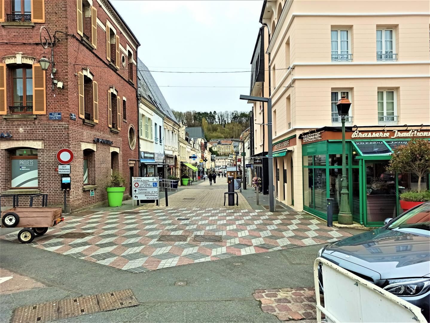 Eine Straße mit Schachbrettmuster-Belag, Häuser mit Geschäften und einer Bushaltestelle.