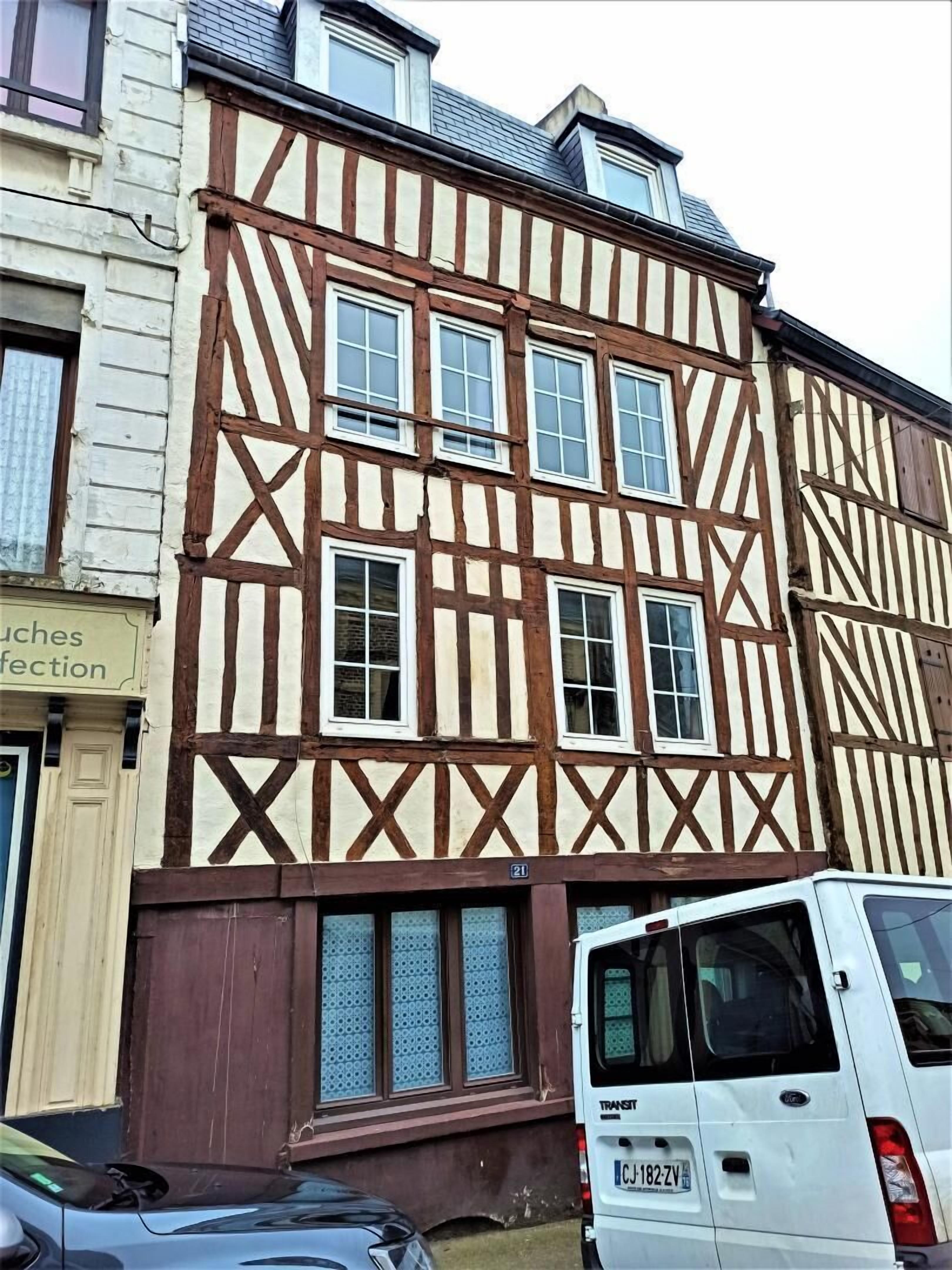 Un edificio tradicional con entramado de madera y varias ventanas, con una furgoneta blanca estacionada adelante.